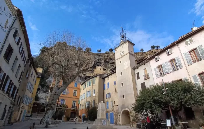 la plus belle place de cotignac sous un beau ciel bleu avec des maisons troglodytes sur les hauteurs